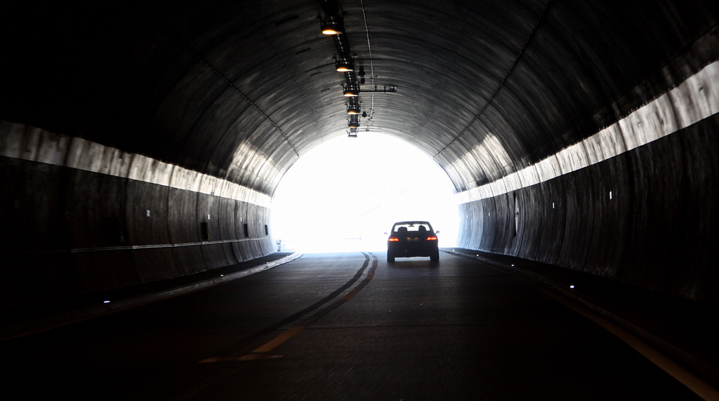 A car driving toward the light at the end of a tunnel.